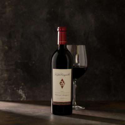 Single bottle of Cabernet with a wine glass behind the bottle against a dark gray background.