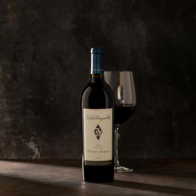 Single bottle of red wine with a wine glass behind the bottle against a dark gray background.